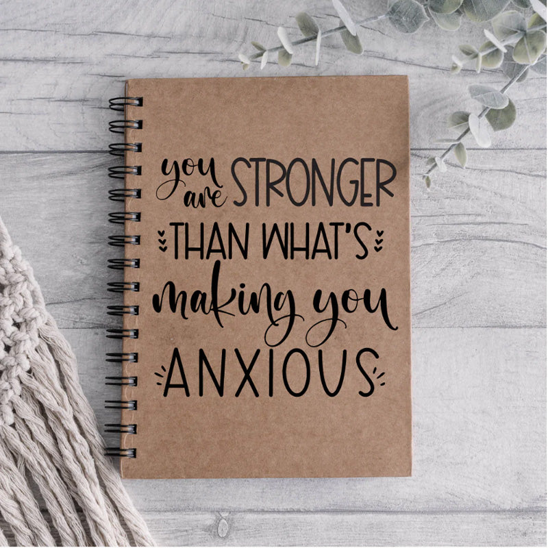 A brown ring bound notebook with the cover reading 'you are stronger than what's making you anxious'.